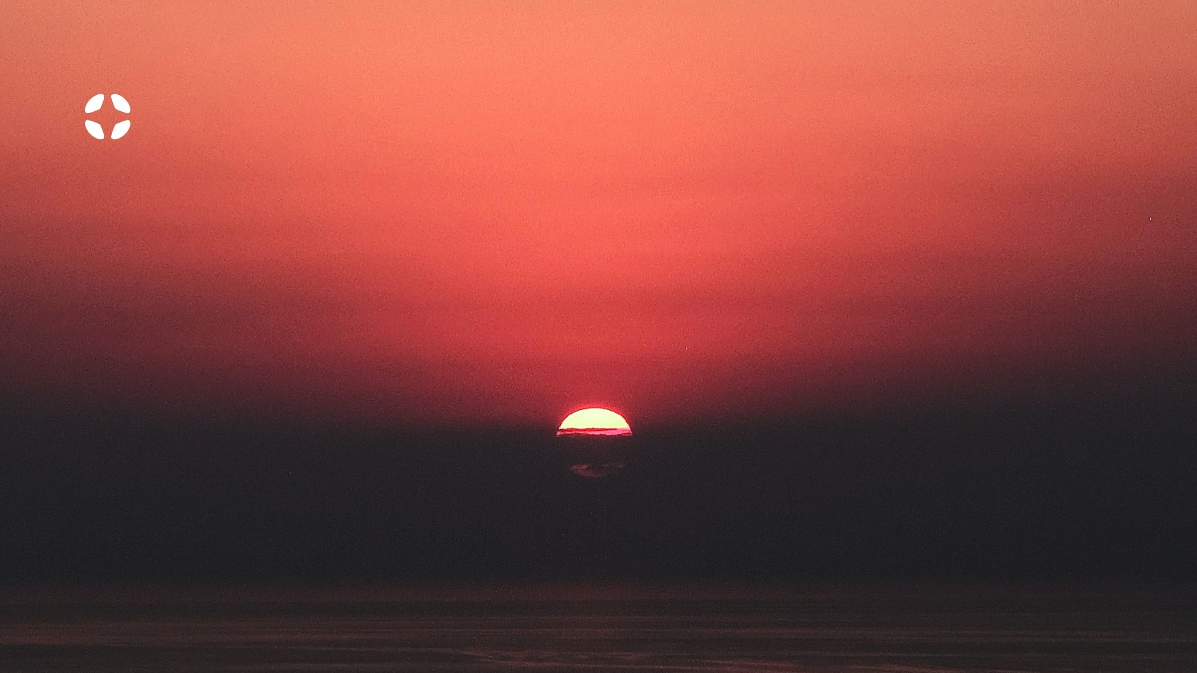 The sun going down into the sea, with the Evallot icon in white
